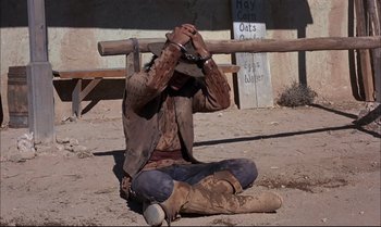 Movie still from “Billy Two Hats” (1974), directed by Ted Kotcheff – A man sitting on the ground with his head down; Wide shot, High angle