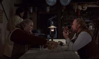 Movie still from “Billy Two Hats” (1974), directed by Ted Kotcheff – Two men sitting at a table with a bottle of wine; Medium shot, Over the shoulder angle