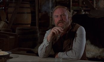 Movie still from “Billy Two Hats” (1974), directed by Ted Kotcheff – An older man sitting at a table smoking a cigarette; Close Up shot, Low angle