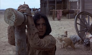 Movie still from “Billy Two Hats” (1974), directed by Ted Kotcheff – A woman holding onto a fence post while standing next to chickens; Medium shot, Low angle