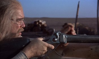 Movie still from “Billy Two Hats” (1974), directed by Ted Kotcheff – A man with a pair of glasses is working on something; Close Up shot, Low angle