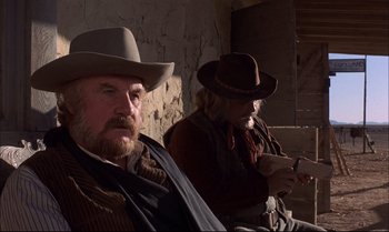 Movie still from “Billy Two Hats” (1974), directed by Ted Kotcheff – Two men sitting next to each other wearing hats; Medium shot, Low angle