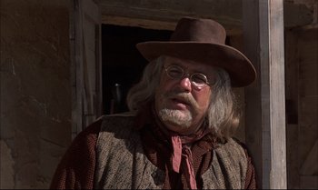 Movie still from “Billy Two Hats” (1974), directed by Ted Kotcheff – An old man with a long beard wearing a hat and glasses; Close Up shot, Low angle