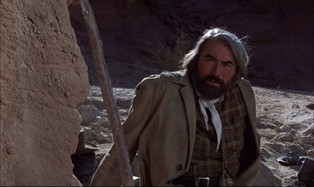 Movie still from “Billy Two Hats” (1974), directed by Ted Kotcheff – A man with a long beard wearing a jacket and a hat; Medium shot, Low angle