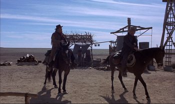 Movie still from “Billy Two Hats” (1974), directed by Ted Kotcheff – Two men on horses in a dirt field; Wide shot, Low angle
