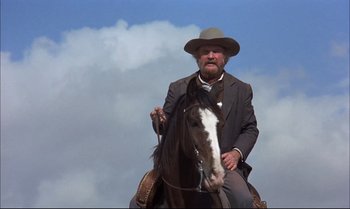 Movie still from “Billy Two Hats” (1974), directed by Ted Kotcheff – An old man sitting on top of a brown horse; Medium shot, Low angle