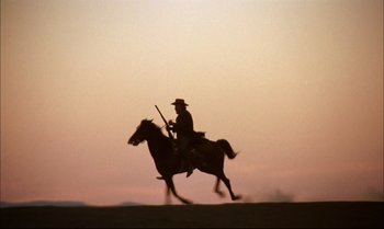 Movie still from “Billy Two Hats” (1974), directed by Ted Kotcheff – A man riding on the back of a brown horse; Wide shot, Low angle