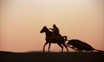 Movie still from “Billy Two Hats” (1974), directed by Ted Kotcheff – A man riding a horse drawn carriage across a field at sunset; Wide shot, Low angle