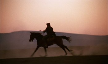 Movie still from “Billy Two Hats” (1974), directed by Ted Kotcheff – A man riding on the back of a brown horse; Wide shot, Low angle