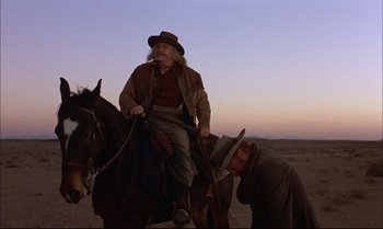 Movie still from “Billy Two Hats” (1974), directed by Ted Kotcheff – A man sitting on top of a horse while another man stands next to it; Medium shot, Low angle
