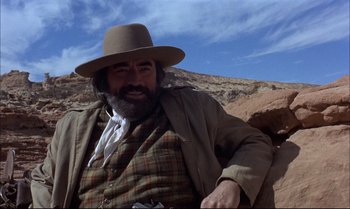 Movie still from “Billy Two Hats” (1974), directed by Ted Kotcheff – A man with a beard wearing a hat and a jacket; Medium shot, Low angle