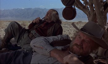 Movie still from “Billy Two Hats” (1974), directed by Ted Kotcheff – Two men in cowboy hats are sitting on the ground; Medium shot, Low angle