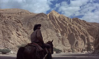 Movie still from “Billy Two Hats” (1974), directed by Ted Kotcheff – A man riding a horse in front of a mountain range; Wide shot, Low angle