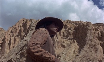 Movie still from “Billy Two Hats” (1974), directed by Ted Kotcheff – A man wearing a cowboy hat standing on top of a mountain; Medium shot, Low angle