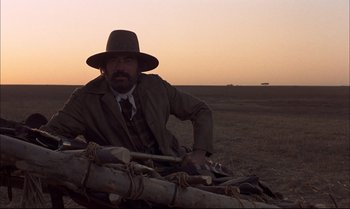 Movie still from “Billy Two Hats” (1974), directed by Ted Kotcheff – A man sitting on top of a pile of logs; Wide shot, Low angle