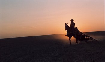 Movie still from “Billy Two Hats” (1974), directed by Ted Kotcheff – A man riding on the back of a horse in a field; Wide shot, Low angle