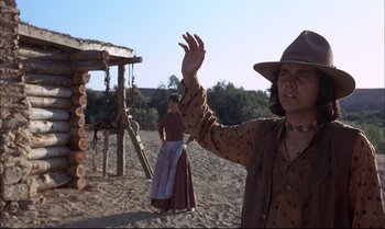 Movie still from “Billy Two Hats” (1974), directed by Ted Kotcheff – A woman in a cowboy hat waves at the camera while another woman stands in the background in front of a swing set; Medium shot, Low angle