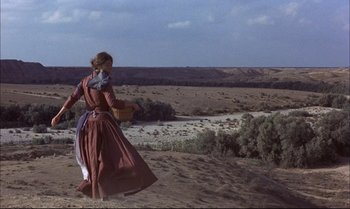 Movie still from “Billy Two Hats” (1974), directed by Ted Kotcheff – A woman walking on a dirt road near a river; Wide shot, High angle