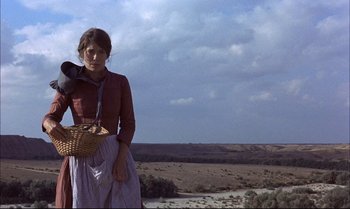 Movie still from “Billy Two Hats” (1974), directed by Ted Kotcheff – A woman standing in a field holding a basket; Wide shot, Low angle