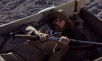 Movie still from “Billy Two Hats” (1974), directed by Ted Kotcheff – A man with a beard and a cowboy hat is holding a rifle; Medium shot, Overhead angle