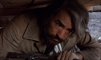 Movie still from “Billy Two Hats” (1974), directed by Ted Kotcheff – A man with long hair and a beard leaning against a wall with a gun; Close Up shot, Low angle