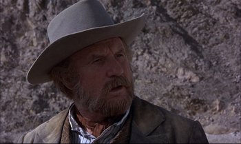 Movie still from “Billy Two Hats” (1974), directed by Ted Kotcheff – An older man wearing a gray hat and a brown jacket; Close Up shot, Low angle