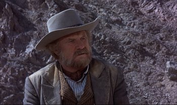 Movie still from “Billy Two Hats” (1974), directed by Ted Kotcheff – An old man with a gray hat and a beard; Close Up shot, Over the shoulder angle