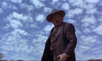 Movie still from “Billy Two Hats” (1974), directed by Ted Kotcheff – An old man in a suit and hat is holding a gun; Medium shot, Low angle