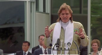 Movie still from “Bio-Dome” (1996), directed by Jason Bloom – A man with long hair is giving a speech at a podium; Close Up shot, Low angle