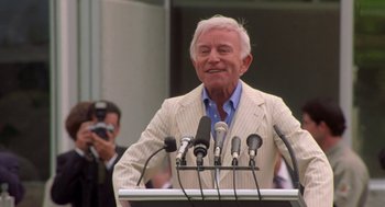 Movie still from “Bio-Dome” (1996), directed by Jason Bloom – An older man standing at a podium with microphones in front of him; Medium shot, Low angle