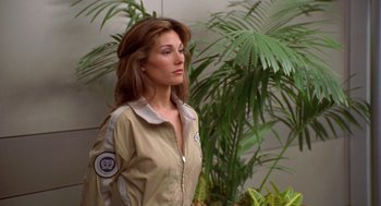 Movie still from “Bio-Dome” (1996), directed by Jason Bloom – A woman in a tan jacket standing in front of a plant; Close Up shot, Over the shoulder angle