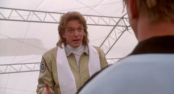 Movie still from “Bio-Dome” (1996), directed by Jason Bloom – A man with long blonde hair wearing a white scarf; Close Up shot, Over the shoulder angle