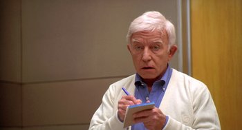 Movie still from “Bio-Dome” (1996), directed by Jason Bloom – An older man writing on a notepad with a pen; Close Up shot, Over the shoulder angle