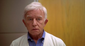 Movie still from “Bio-Dome” (1996), directed by Jason Bloom – An older man in a blue shirt and a white sweater; Close Up shot, Low angle