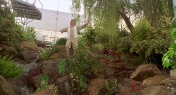 Movie still from “Bio-Dome” (1996), directed by Jason Bloom – A man standing on top of a rock in a garden; Wide shot, Low angle