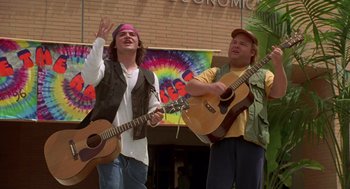 Movie still from “Bio-Dome” (1996), directed by Jason Bloom – Two men are singing and playing guitars in front of a crowd of onlookers; Medium shot, Low angle