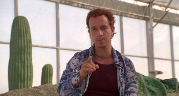 Movie still from “Bio-Dome” (1996), directed by Jason Bloom – A man sitting in front of a window with a cactus in the background; Close Up shot, Low angle