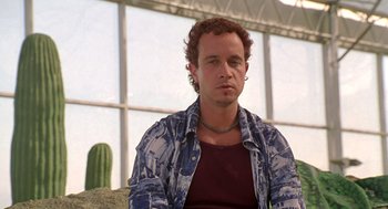 Movie still from “Bio-Dome” (1996), directed by Jason Bloom – A man sitting in front of a large window; Close Up shot, Low angle