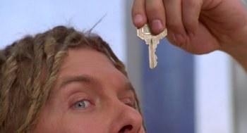 Movie still from “Bio-Dome” (1996), directed by Jason Bloom – A person holding a key in front of their face; Extreme Close Up shot, Overhead angle
