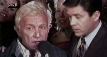 Movie still from “Bio-Dome” (1996), directed by Jason Bloom – An older man is speaking into a microphone; Close Up shot, High angle