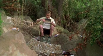 Movie still from “Bio-Dome” (1996), directed by Jason Bloom – A man sitting on the ground with a box in front of him; Medium shot, Low angle