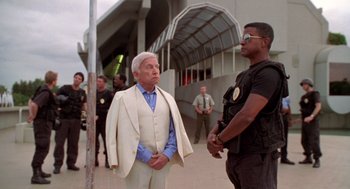 Movie still from “Bio-Dome” (1996), directed by Jason Bloom – A man in a white suit is talking to a police officer; Medium shot, Low angle