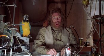 Movie still from “Bio-Dome” (1996), directed by Jason Bloom – A man with long hair and a beard sitting at a table with a parrot; Close Up shot, Low angle