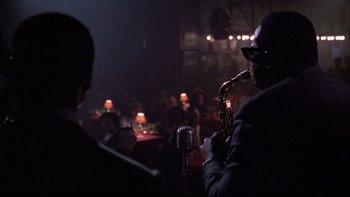 Movie still from “Bird” (1988), directed by Clint Eastwood – A man playing a saxophone in front of an audience; Medium shot, Over the shoulder angle