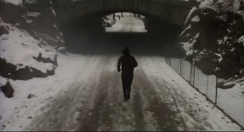 Movie still from “Birth” (2004), directed by Jonathan Glazer – A person is walking down a snow covered road; Wide shot, High angle