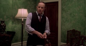 Movie still from “Birth” (2004), directed by Jonathan Glazer – A man in a suit and tie holding a knife; Medium shot, Low angle