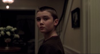 Movie still from “Birth” (2004), directed by Jonathan Glazer – A young boy with short hair is standing in a room; Close Up shot, Over the shoulder angle
