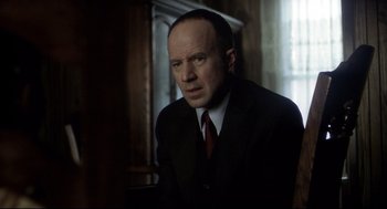 Movie still from “Birth” (2004), directed by Jonathan Glazer – A man wearing a suit and tie sitting in a room; Close Up shot, Over the shoulder angle