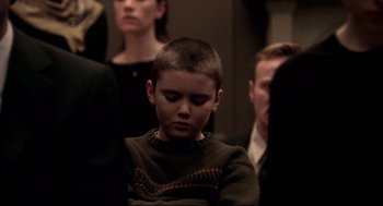 Movie still from “Birth” (2004), directed by Jonathan Glazer – A young boy is sitting in a crowd of people; Medium shot, Over the shoulder angle