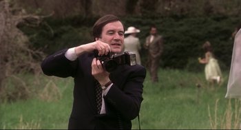 Movie still from “Birth” (2004), directed by Jonathan Glazer – A man in a suit and tie holding a camera in a field; Close Up shot, Low angle
